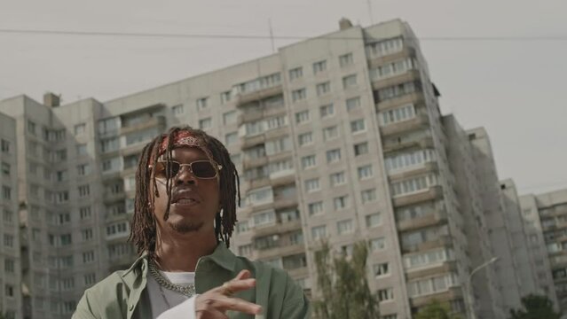 Medium shot of African American guy with dreadlocks rapping at camera in street at daytime