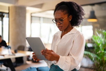 Upset African businesswoman in office. Young tired woman using digital tablet..