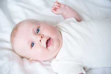healthy smiling baby lies on his back on bed on white bedding. top view