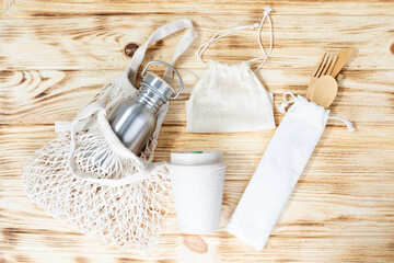 Different fabric bags for storage on a light wooden background. Eco bags for multiple use. A reusable wooden cutlery, mug and bottle. Flat lay