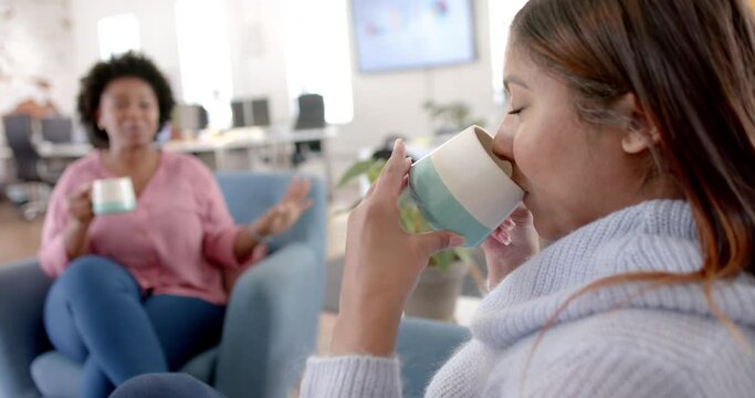 Diverse business female colleagues drinking coffee and talking in office, slow motion