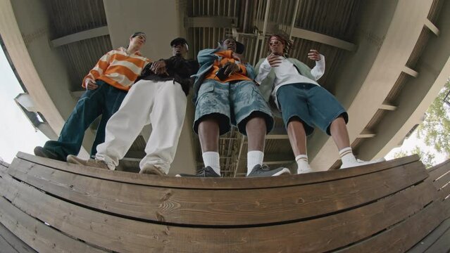 Low angle stab shot of four diverse dudes in streetwear dancing tp hip hop music under city bridge at daytimeLow angle stab shot of four diverse dudes in streetwear dancing tp hip hop music under city