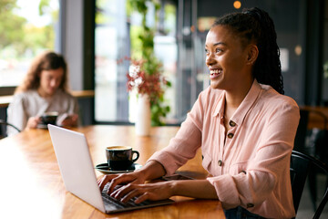 Young Businesswoman With Coffee Working On Laptop Sitting In Cafe Or Office With Colleague In Background