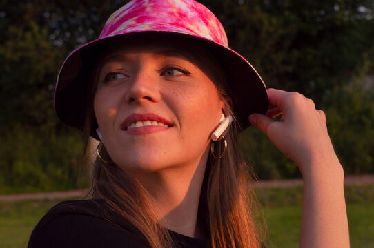 beautiful young girl with freckles in a bright hat listens to music in white air poods