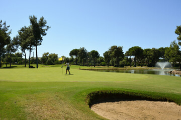 A young woman on the green of a private golf club adjusts the flag near the hole