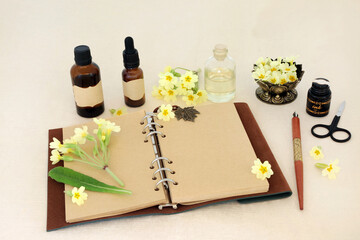Preparation of primula flowers for natural essences with notebook and essential oil bottles. Floral healthcare concept for flower remedies on hemp paper. Used to treat insomnia, bronchitis, asthma. 