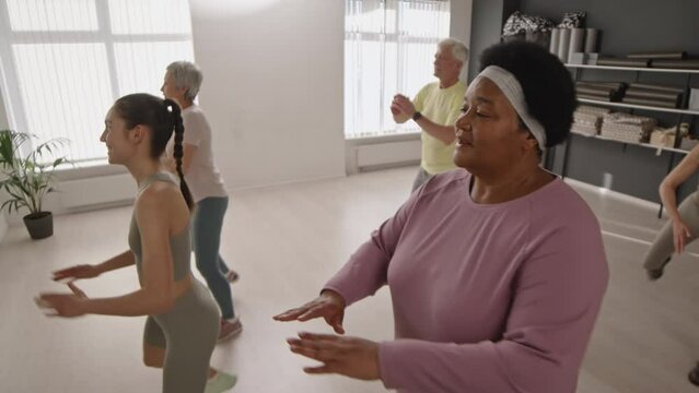 Group of senior people in sportswear doing butt kick exercise with young female fitness trainer during aerobics class in studio