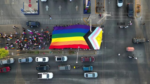 the lgbt community marches through the streets of the city showing a giant Progress Pride Flag with hundreds of people carrying it with pride