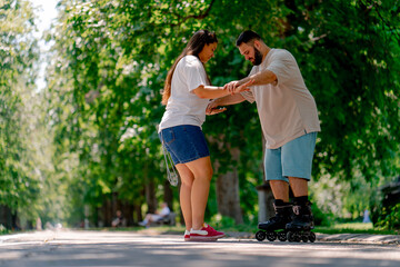 Obraz premium Young couple girl holds hands of the guy who is roller skating and helps him to learn to skate in the park plus size models
