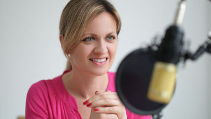 Beautiful smiling woman speaks into microphone at workplace. Working radio presenter