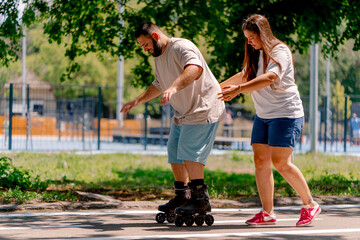 Obraz premium Young couple girl holds hands of the guy who is roller skating and helps him to learn to skate in the park plus size models