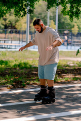 Obraz premium Young guy with a beard learns to rollerblade in a city park concept of wanting to learn new things and body positivity 