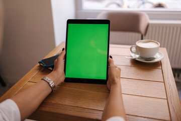 First person view of female hold digital tablet in cafe. Table with cup of coffee. Mock up of tablet. Green screen