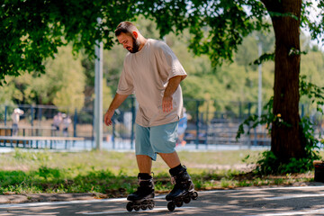 Young guy with a beard learns to rollerblade in a city park concept of wanting to learn new things...