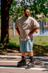Portrait of a young guy tired of rollerblading against the background of trees in the park plus...