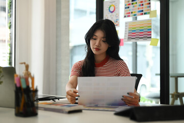 Young creative woman working with color palette, choosing color samples for design project at graphic studio