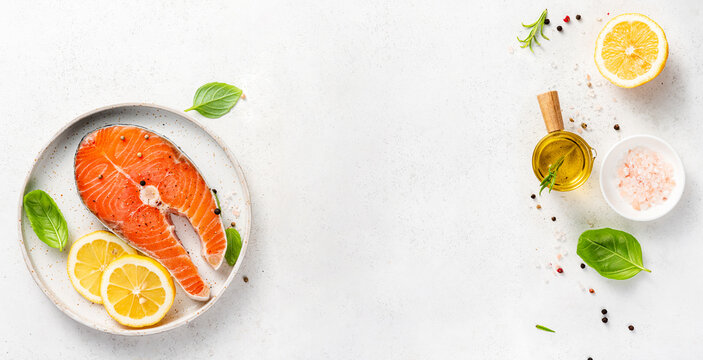 Fresh raw salmon steaks with spices, lemons and pink salt on white plate. Top view of fish with copy space. Keto recipe.