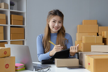 Happy asian businesswoman owner with a parcel box and checking orders from customers, online delivery service warehouse, sell products online concept.