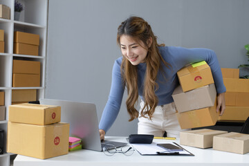 Happy asian businesswoman owner with a parcel box and checking orders from customers, online delivery service warehouse, sell products online concept.