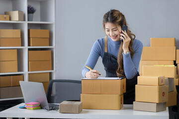 Happy asian businesswoman owner with a parcel box and checking orders from customers, online delivery service warehouse, sell products online concept.