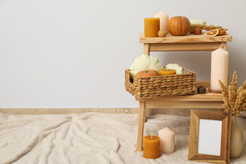 Candles and pumpkins on shelves, photo frame and vase on beige background, space for text