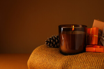 Candle, cones and gifts on sweater on orange background, space for text
