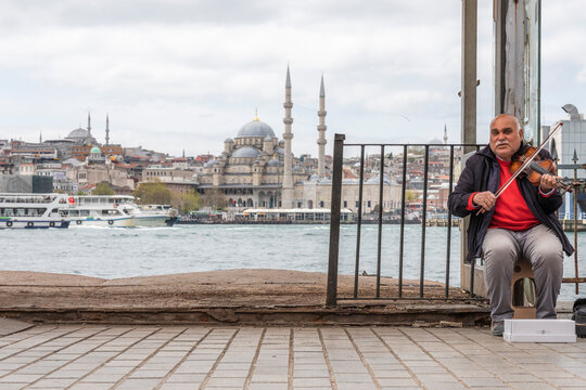 Istanbul, Turkey - 23 April 2023: View of a person playing the violin on the street along the Bosphorus channel with Suleymaniye Mosque in background in Istanbul, Turkey.