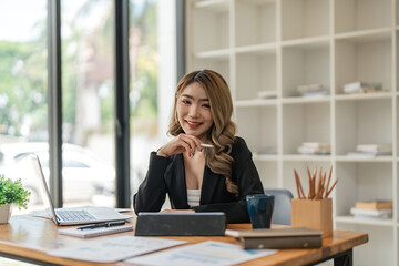 Portrait of young attractive asian woman with relaxing while sitting at her office desk, smiling and looking at camera