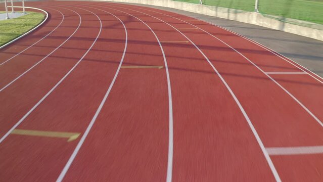 Tour over the red oval athletic track with eight lanes on an outdoor stadium, tracking shot.