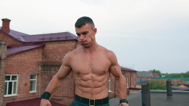Bodybuilder with naked torso points finger at kettlebell and shows his big biceps and puts tabata timer on mobile phone