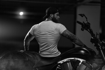 Athletic bearded biker man posing with motorbike with his back to the frame