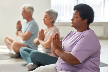 Group of senior people meditating in lotus position in yoga class