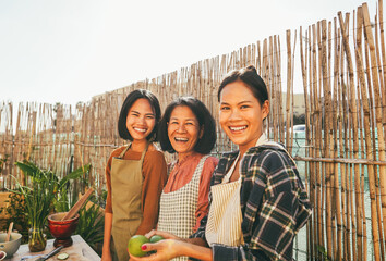 Asian mother with her daughters smiling in front of camera at home terrace - Happy family cooking...
