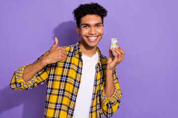 Photo of cheerful nice person toothy smile hand hold roll dollar bills demonstrate thumb up isolated on violet color background