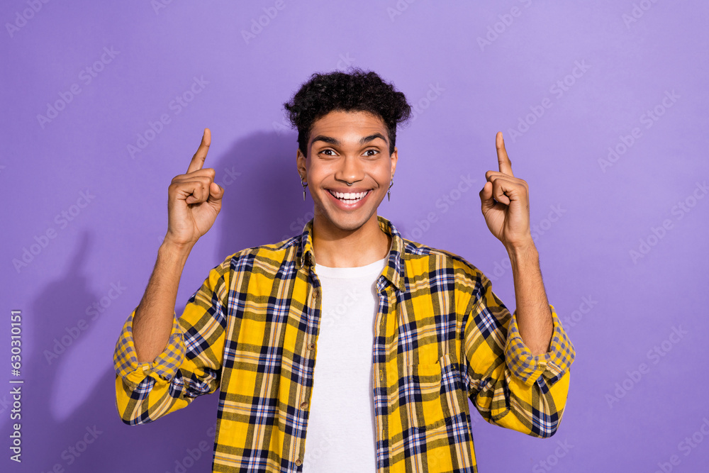 Wall mural Photo of funny funky guy with earrings dressed checkered shirt indicating at offer empty space staring isolated on purple color background