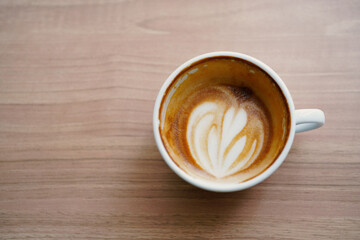 Half cup of hot latte art in heart shaped after drink on wooden table background. Copy space.