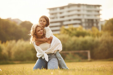 Fototapeta premium Sitting on the mother shoulders. Woman with her little daughter are on the summer field together