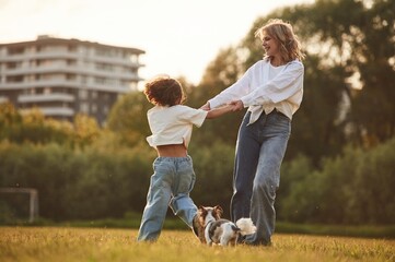 Obraz premium Beautiful mother with her little daughter and dog are on the summer field together