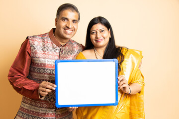 Happy indian couple wearing traditional outfit holding blank place card to put message isolated on...