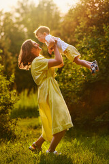 A mother woman plays with a child in nature, lifting and tossing him in her arms. Toddler baby and...