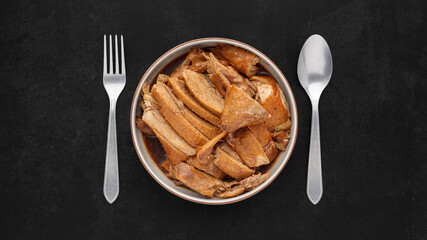 brown Chinese stewed calf of duck leg in ceramic bowl with fork and spoon on dark tone texture background, top view, flat lay, full HD ratio, Thai food, Ped Pa Lo, Ped Palo, Ped Palow