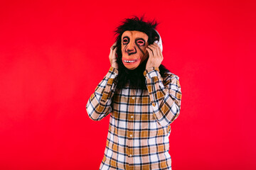 Man with chimpanzee monkey mask and checkered shirt, listening to music with white headphones, on...