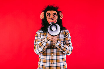 Fototapeta premium Man with chimpanzee monkey mask and plaid shirt, shouting with a megaphone, on red background.