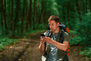 Big backpack and smartphone. Tourist in summer forest. Conception of exploration and leisure