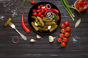 Assorted pickled vegetables in a black plate on a dark background.