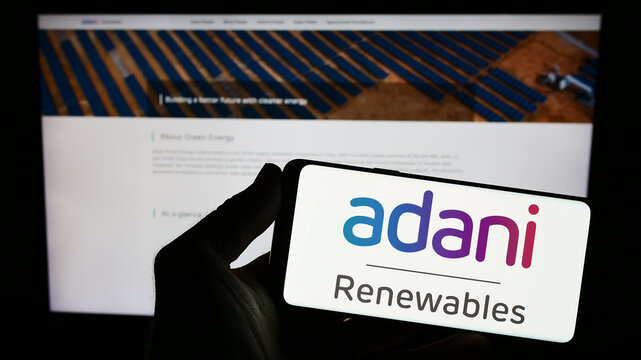 Stuttgart, Germany - 07-26-2023: Person holding smartphone with logo of Indian company Adani Green Energy Limited on screen in front of website. Focus on phone display.