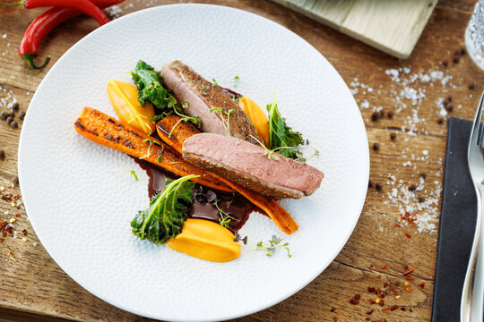 Duck fillet with sweet potato cream, roasted carrots, kale, beet-port sauce on white plate. Grilled and roasted poultry closeup served on a table for lunch in modern cuisine gourmet restaurant.