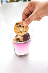 Assorted cookies in a plastic container to go cup, hand lifting one cookie out, sticker template placed for branding.