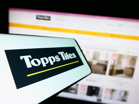 Stuttgart, Germany - 07-27-2023: Mobile phone with logo of British retail company Topps Tiles plc on screen in front of business website. Focus on center-left of phone display.