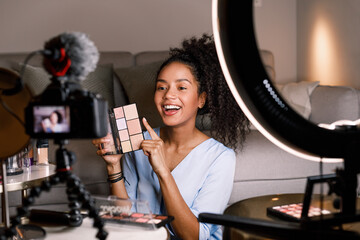 Laughing female holding an eyeshadow palette while filming a video for her beauty vlog